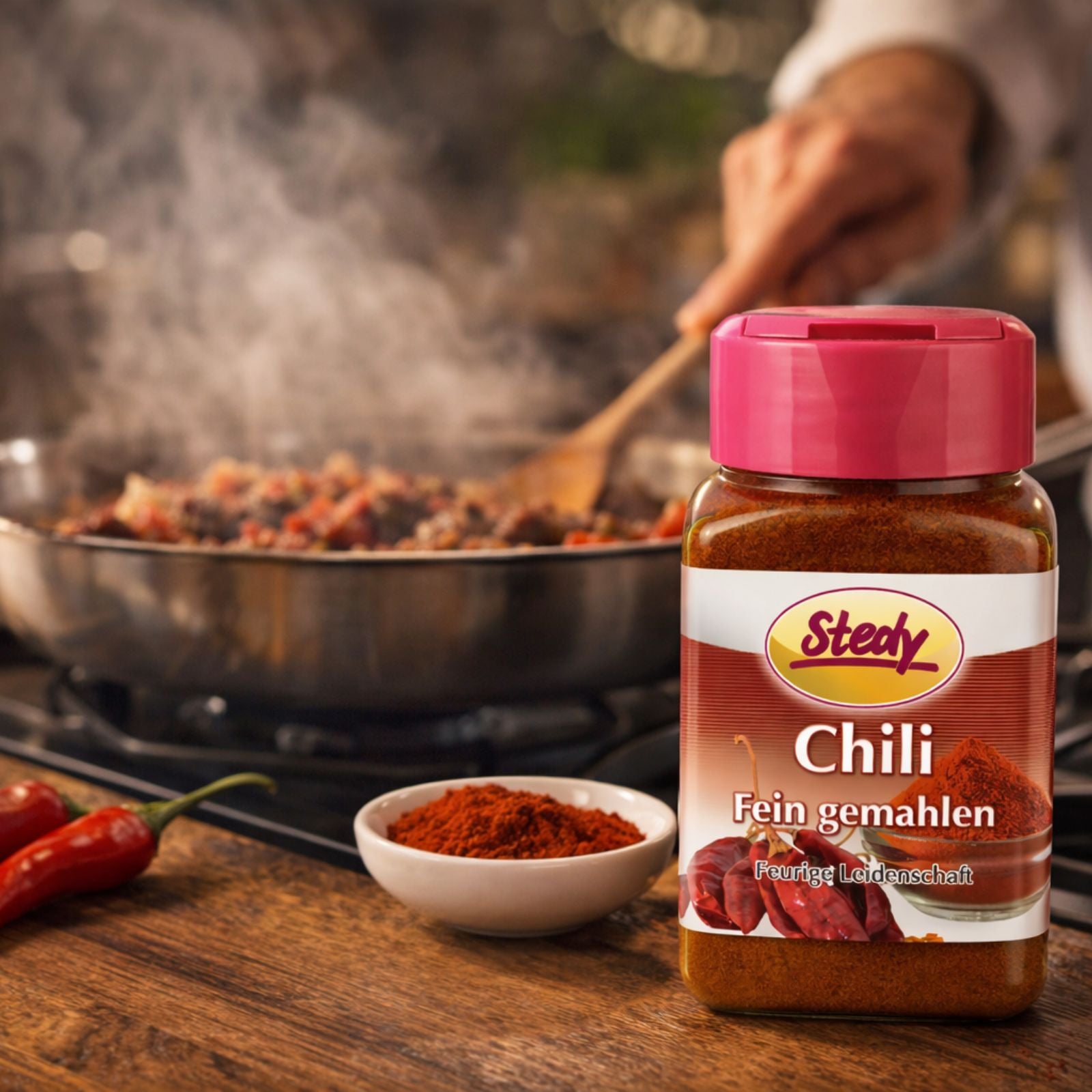 Chilipulver im Streuer beim Kochen in Pfanne, würzige Küchenszene mit Dampf